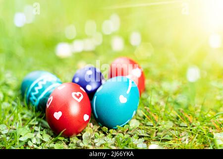 Beautiful painted real easter eggs lie in the fresh spring grass. The sun is shining. Red and turquoise eggs are decorated with white ornaments. Stock Photo