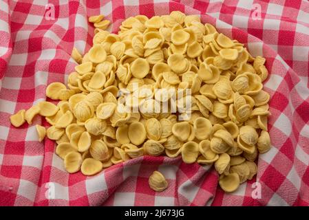 Orecchiette on red checkered tablecloth, Italian pasta from Puglia made with durum wheat flour and water, typical of the Apulian cuisine Stock Photo
