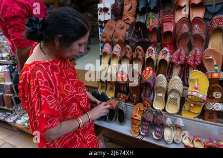 Jaisalmer, Rajasthan, India - October 13, 2019 : Indian woman checking pairs of Rajasthani womens' shoes at display for sale. Jaisalmer, Rajasthan, In Stock Photo