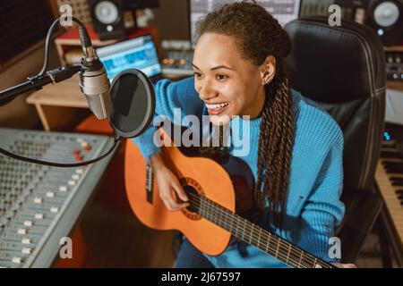 Passionate African American woman singer playing the guitar and recording song in professional studio Stock Photo