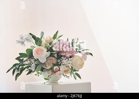 A composition of different flowers in a white vase on a square podium. The concept of a flower shop. A beautiful freshly cut bouquet. Flower delivery. High quality photo Stock Photo