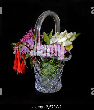 Collection of mixed colourful fresh flowers in a beautiful Cut Glass Basket Vase isolated on a black coloured background. Wall art and decoration imag Stock Photo