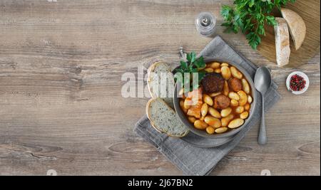Typical Spanish fabada asturiana on wooden table with bread. Top view, copy space Stock Photo