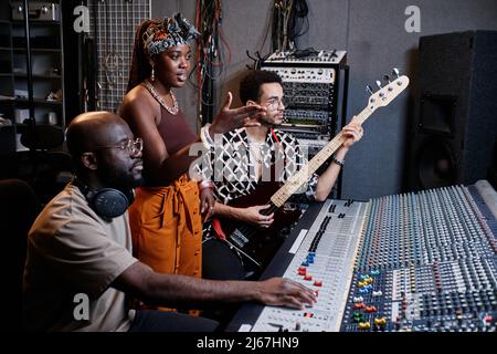 Mature African American music producer, young female singer and male guitarist working on song in recording studio Stock Photo