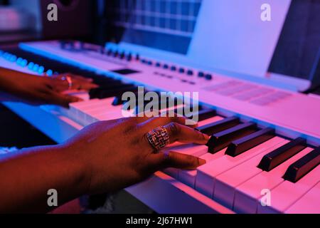 Close-up of unrecognizable Black womans hands playing electronic keyboard in blue and pink neon light Stock Photo