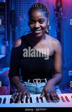 Vertical medium portrait of young Black woman with digital keyboard in recording studio smiling at camera Stock Photo