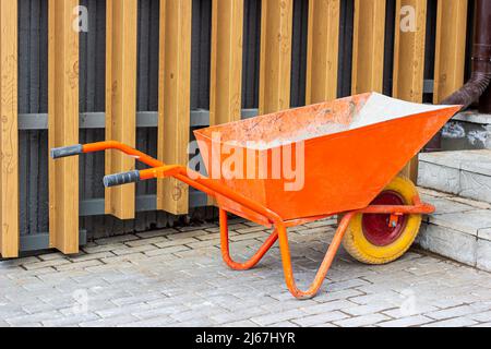 Bright orange wheelbarrow cart for gardening and construction site on the street. Stock Photo