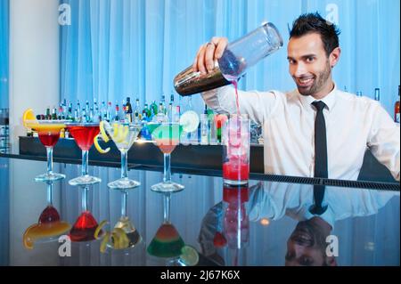 Bartender smiling at the camera while pouring drinks. Stock Photo