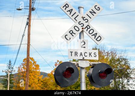 Railroad crossing sign with lights on a partly cloudy autumn day. An electricity post is in background. Stock Photo