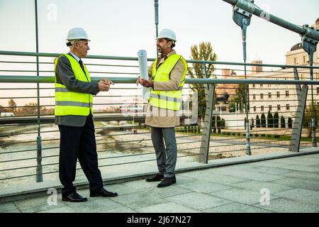 Two senior construction managers are standing on the bridge while talking about the new plans Stock Photo
