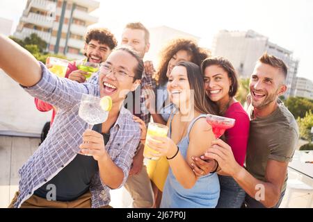 Happy selfie with people drinking alcohol cocktails in a terrace bar. Celebrating birthday of a best friends. Stock Photo