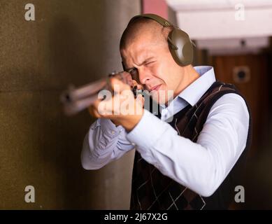 Concentrated man practicing shotgun shooting at firing range Stock Photo