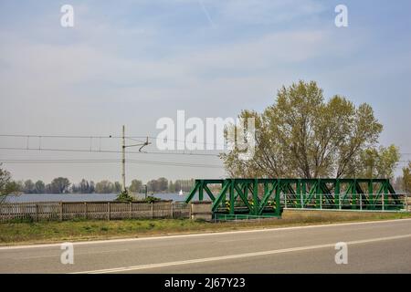 Road next to a lake and a park with railroad tracks by its edge on a sunny day Stock Photo