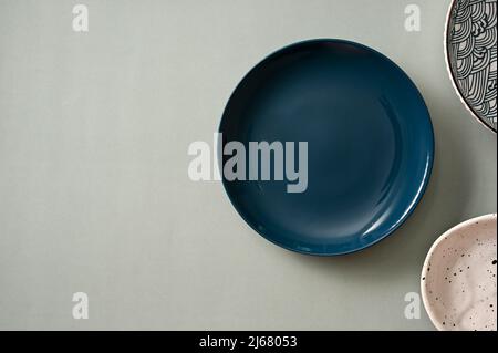 Minimal stylish dining table setting with minimal dark blue plate and handcraft ceramic plates on grey background. top view Stock Photo