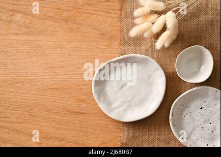 Minimal dining table setting with ceramic handcraft white plates on brown place mat and space on wood table. top view Stock Photo