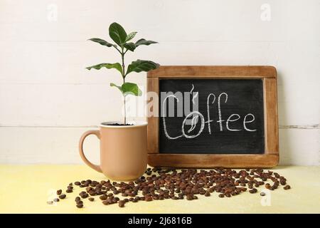 Chalkboard with word COFFEE, young tree and beans on wooden table Stock Photo