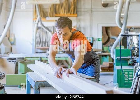Focused carpenter sanding wooden detail in workshop Stock Photo