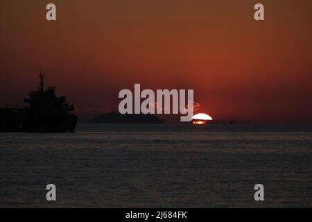 Last seconds of a sunset over sea, with a big ship and a distant island seen as silhouettes Stock Photo