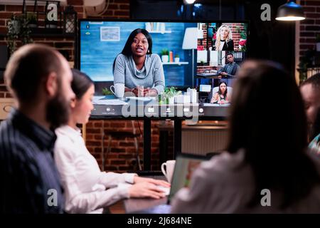 Multiethnic startup team in online video call with colleagues working remote doing overtime working late at the office. Workaholic coworkers doing teamwork brainstorming in group project conference. Stock Photo