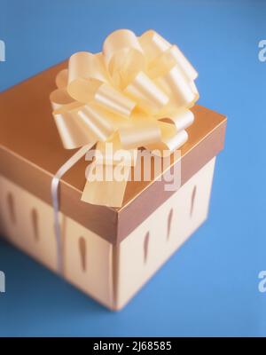 Gold colored gift box with ribbon isolated on blue background Stock Photo