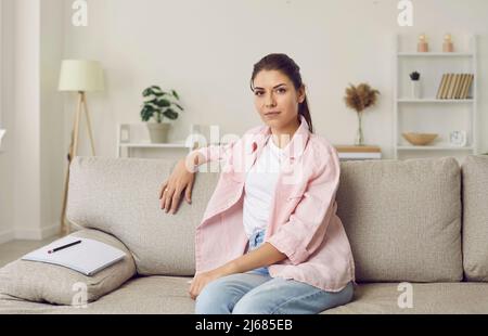 Webcam view of serious woman sitting on couch at home, looking at camera and listening Stock Photo