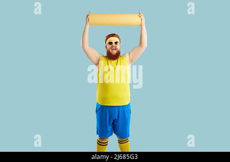 Funny fat man cheerfully lifts up sports mat rejoicing that he has finished doing sports training. Stock Photo