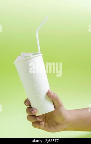 Human hand holding a white plastic cup with ice cubes and a straw with colored background Stock Photo