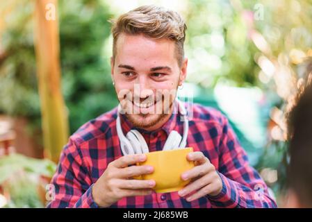 Happy male in checkered shirt smiling and looking away while enjoying fresh coffee in morning in yard Stock Photo