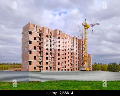 Residential brick house under construction. Unfinished house and tower crane. New multi-storey building. Stock Photo