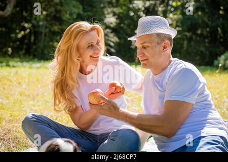 Joyful caucasian couple sits in city park. Man and woman outdoors, hugging, smiling and laughing on a sunny summer day in casual light clothes. Happy couple retired concept Stock Photo