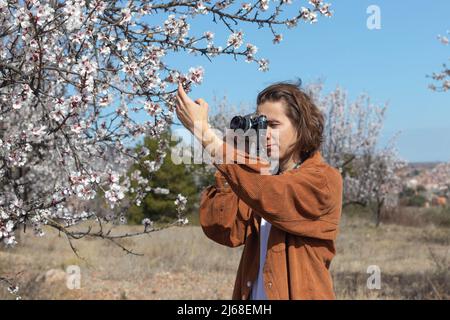 Young man taking pictures of flowers with a retro camera on a field trip and beautiful scenery in the background Stock Photo