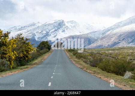 asphalt or tarred endless road leading towards snow covered mountains landscape in Ceres, Western Cape, South Africa during Winter Stock Photo