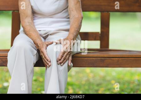 Senior woman sitting on bench, holding her painful knee Stock Photo