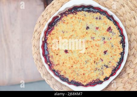 Berry crumble pie in baking dish on natural placemat on a table. summer dessert. cobbler pie with fresh garden grown berries Stock Photo