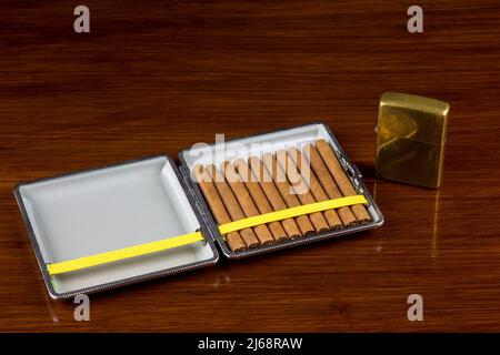 Small cigars in cigar case on old varnished wooden surface with old brass lighter Stock Photo