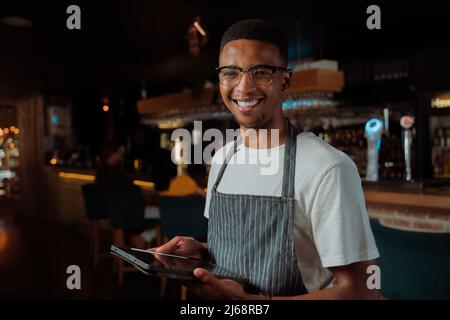 African American male waiter smiling holding digital tablet Stock Photo