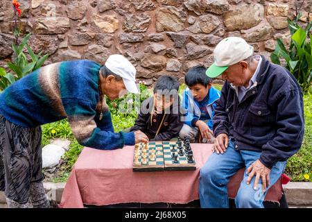 Two Men Playing Chess Watched By Local Children, Pisac, The Sacred Valley, Calca Province, Peru. Stock Photo