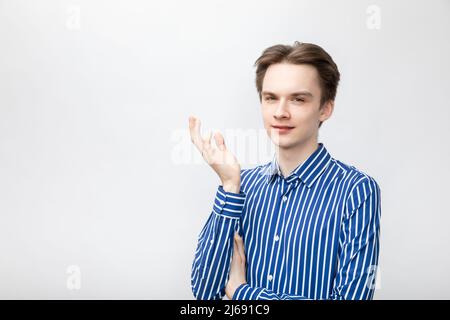 Portrait of doubtful young man wearing blue-white striped button shirt holding hand in questioning gesture looking at camera suspiciously. Studio shot Stock Photo
