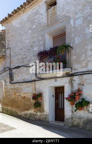 Old house facade, with pots of geraniums hanging on the wall and on its balcony in Fuendetodos, the birthplace of the Spanish painter Francisco De Goy Stock Photo