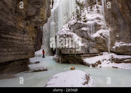 A male wearing red coat stood in Maligne Canyon during winter conditions, Jasper National Park, UNESCO World Heritage Site, Alberta, Canada Stock Photo