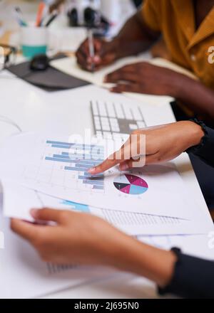 A close up of hands pointing to colourful graph with another person taking notes Stock Photo