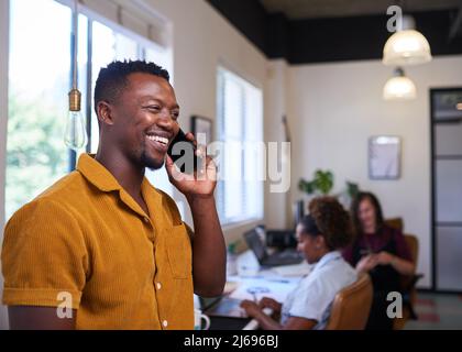 A creative businessman takes a call in the office with colleagues in background Stock Photo