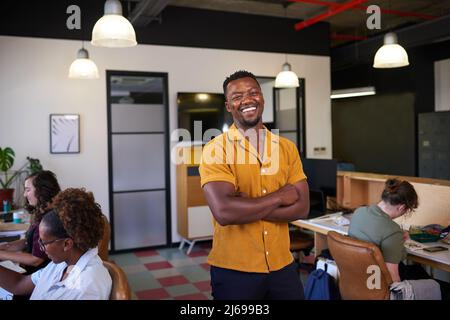 A Black business owner stands with his arms crossed while creative team works Stock Photo