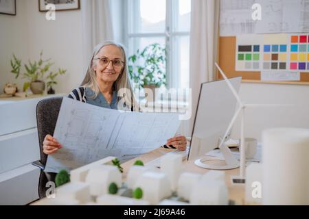 Senior woman eco architect with blueprints working on lapotp in office. Stock Photo
