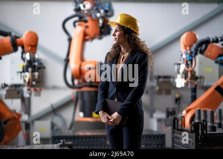 Automation female engineer with tablet for programming robotic arm in factory. Stock Photo
