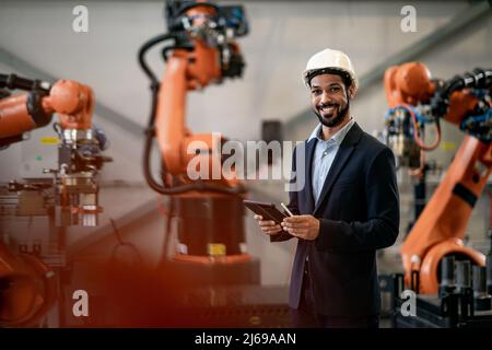 Automation engineer uses tablet for programming robotic arm in factory. Stock Photo