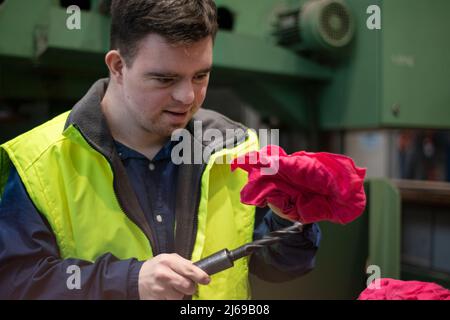 Young man with Down syndrome working in industrial factory, social integration concept. Stock Photo