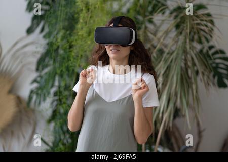 Emotional shocked woman in VR helmet using interactive technology for the first time at home garden Stock Photo