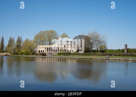 People relaxing around the boating lake at Exhibition Park, Newcastle upon Tyne, UK, with the Wylam Brewery in the background. Stock Photo