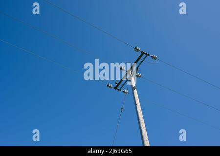 Overhead wooden pole mounted 11kv high voltage three phase electricity distribution cables against a clear blue sky in Somerset, England.. Stock Photo